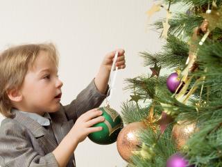 обои Маленький мальчик украшающий елку большой зеленой игрушкой фото