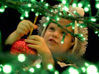 обои Маленькая девочка в шапке украшающая елку красной игрушкой фото