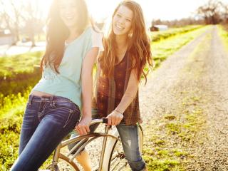 обои Две молоденькие подружки пытаются прокатиться на велосипеде фото